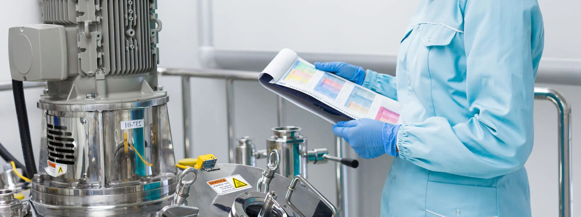 Fachkraft mit Schutzkleidung kontrolliert Qualitätsdaten an Produktionsanlage in der Chemie- und Pharmaindustrie