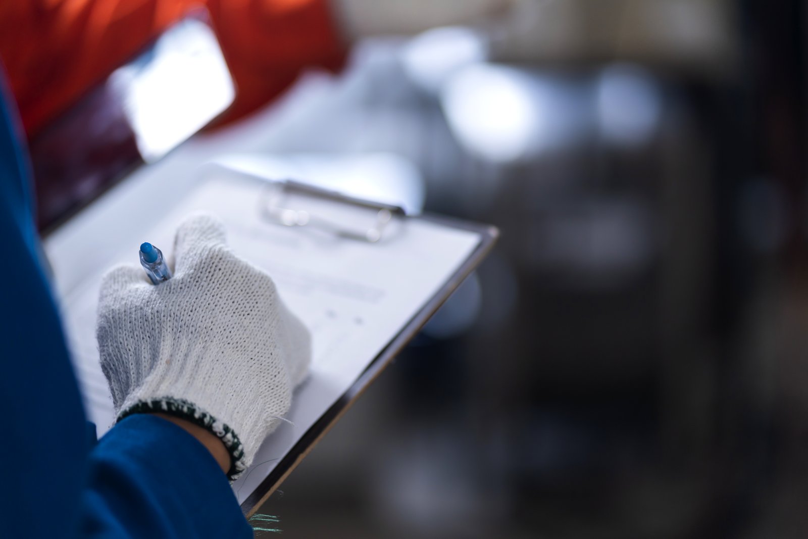 Mitarbeiter mit Arbeitshandschuh dokumentiert die Qualitätskontrolle – Outsourcing per Werkvertrag in der Industrie