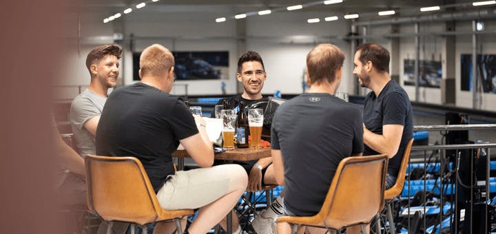 Gruppe von 5 Männern, die an einem Tisch neben der Rennstrecke sitzen und gemeinsam etwas trinken. 