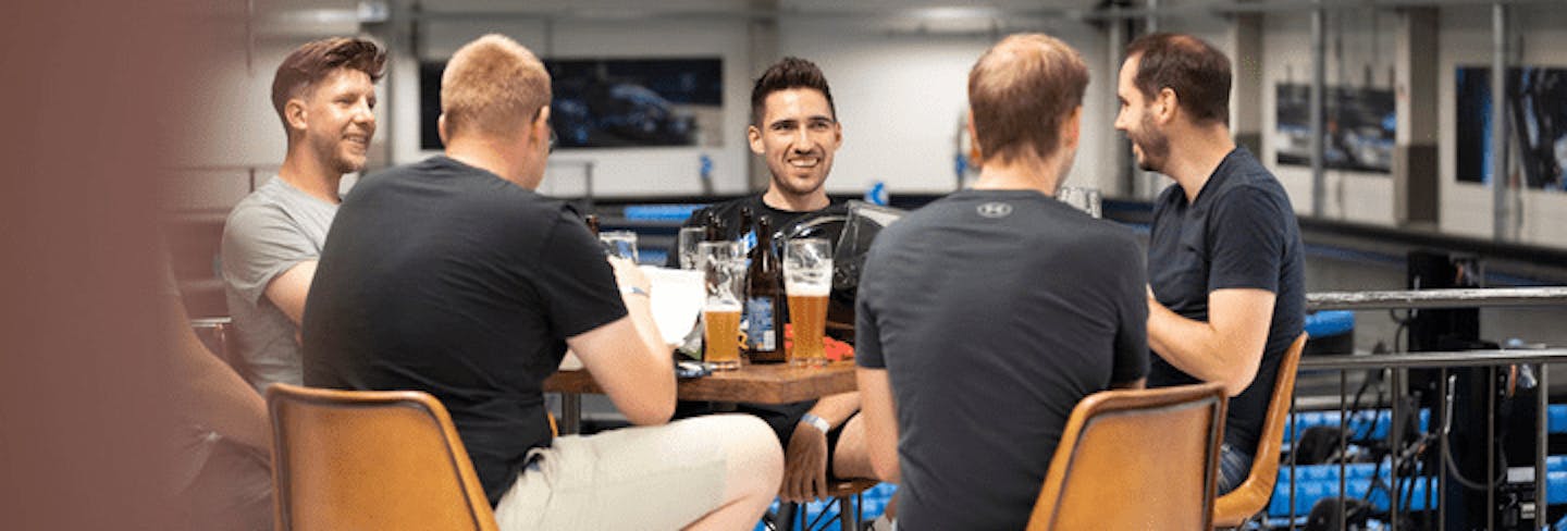 Eine Gruppe von Männern sitzt an einem Tisch vor der Rennstrecke und unterhält sich.