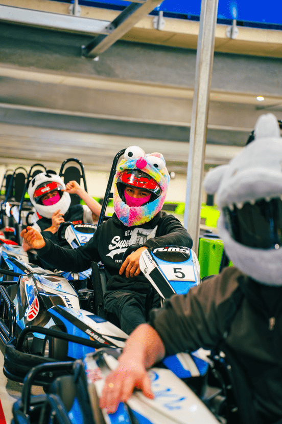 Eine Gruppe von Männern sitzen mit Plüsch-Helm-Covern in ihren Karts in der Boxengasse und sind bereit für den Start