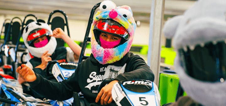 Eine Gruppe von Männern sitzen mit Plüsch-Helm-Covern in ihren Karts in der Boxengasse und sind bereit für den Start