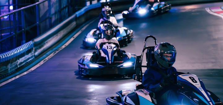 Close-up van een coureur in een kart op de baan. De focus ligt op de kart en de coureur, wat een gevoel van competitie en focus geeft.