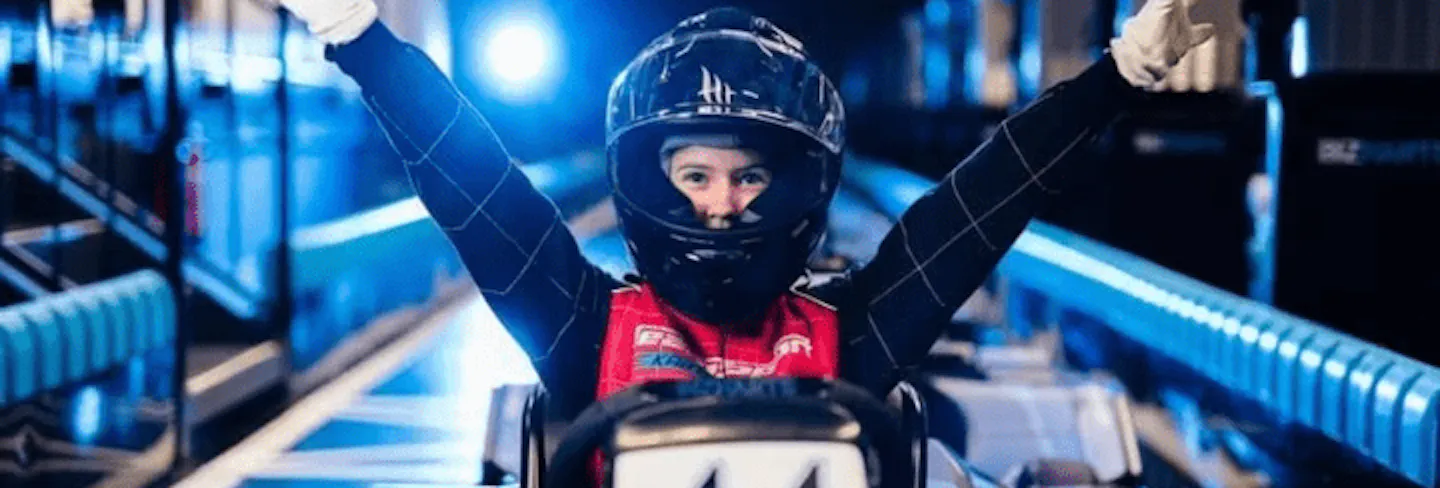 Kid smiling in Electric kart pit lane with arms in the air