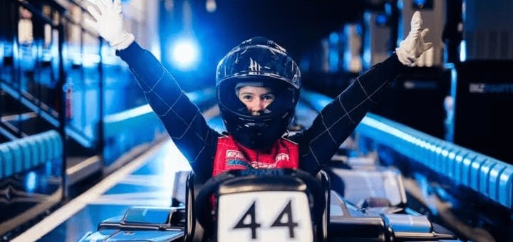 Kid smiling in Electric kart pit lane with arms in the air