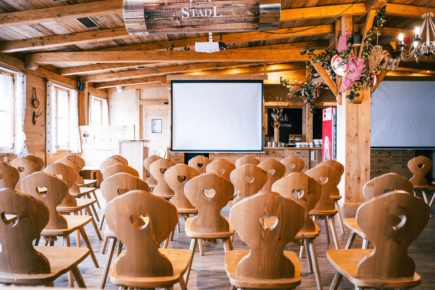 Aufgebaute Sitzreihen im Eventstadl mit einer Leinwand