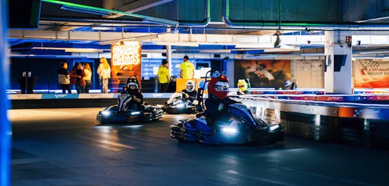 Mehrere Karts fahren auf der Combat Kart Strecke. Einer der Fahrer trägt ein Plüsch-Helm Cover