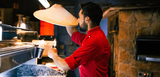 Ein Pizzabäcker schwingt einen Pizzateig durch due Luft