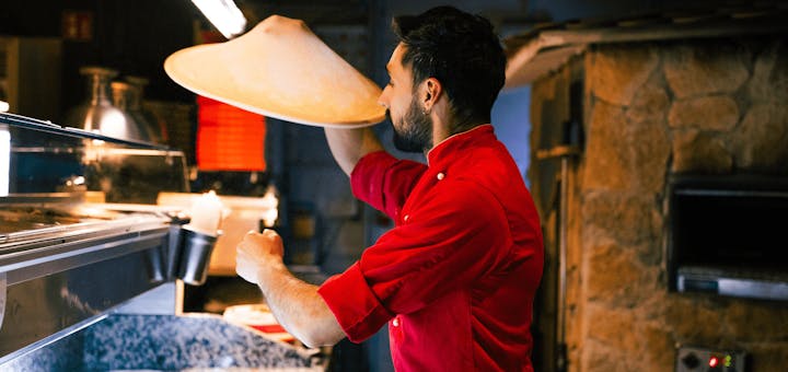 Ein Pizzabäcker schwingt einen Pizzateig durch die Luft