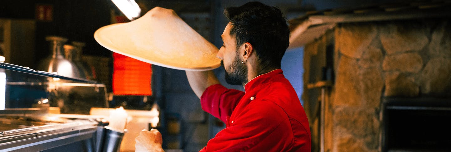Ein Bild von einem Pizzabäcker der den Pizzateig durch die Luft schwingt