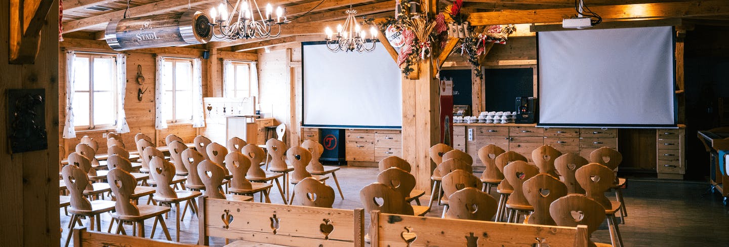 Aufgebaute Sitzreihen vor zwei Leinwänden im Eventstadl