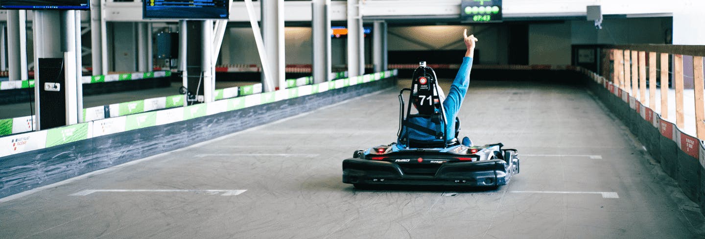 Ein Kartfahrer fährt auf der Start-Ziel- Geraden auf Raceway 3 und hebt siegessicher die Hand