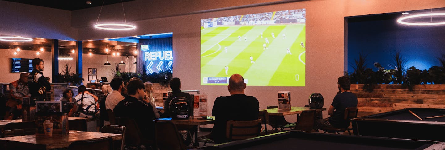 A group of people watching football on a large screen enjoying food and drink