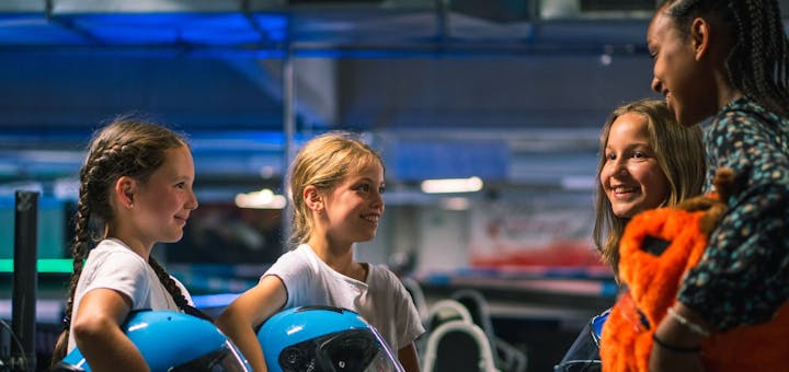 Vier Mädchen mit Helmen in der Hand stehen an der Rennstrecke und haben Spaß!