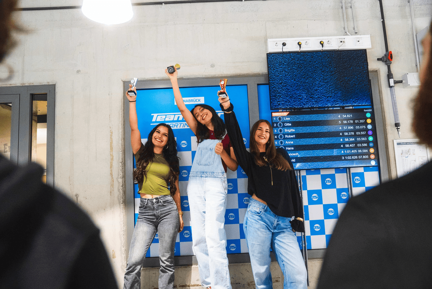 3 Frauen auf dem Siegerpodest. Sie jubeln und haben Pokale in der Hand