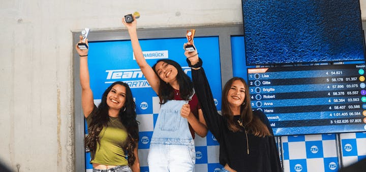 3 Frauen auf dem Siegerpodest. Sie jubeln und haben Pokale in der Hand