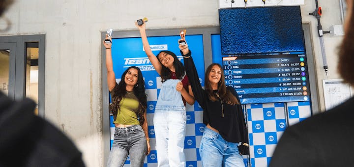 3 Frauen auf dem Siegerpodest. Sie jubeln und haben Pokale in der Hand