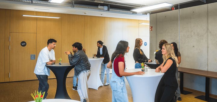 Eine Gruppe von Menschen steht an Hochtischen und unterhält sich!