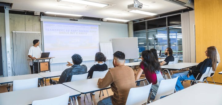 Eine Gruppe schaut einer Präsentation im Meeting Raum zu.