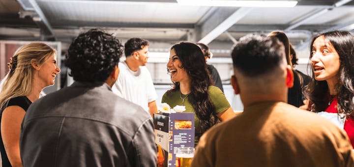 Eine Gruppe steht auf der Aussichtsplattform an den Tischen und unterhält sich.