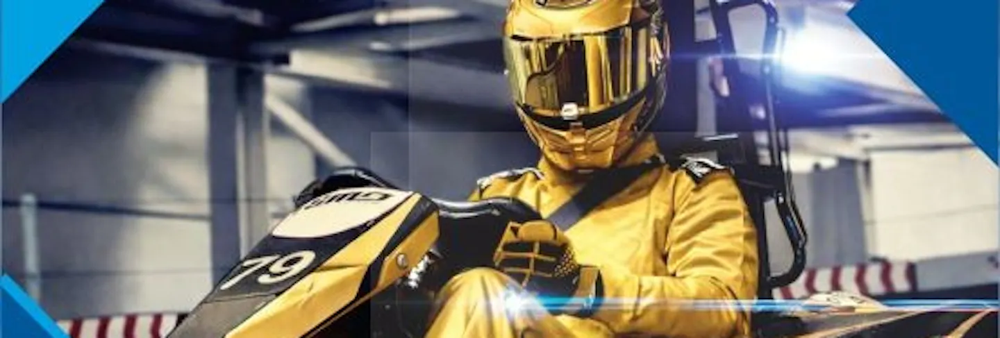 Ein Rennfahrer in einem goldenen Rennanzug mit Helm sitzt im Go Kart