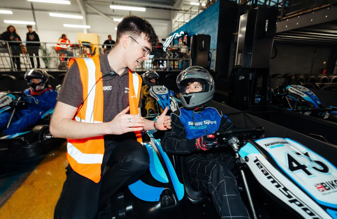 Kid in go kart being coached by a member of staff in the pit lane