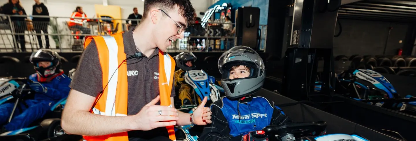 Kid in go kart being coached by a member of staff in the pit lane