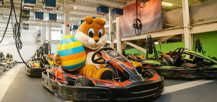 Osterhase sitzt im Kart und hält ein Osterei im Arm