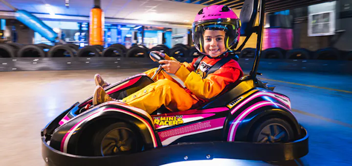 Mini racer aged 4โ7 driving a go kart and smiling on the track