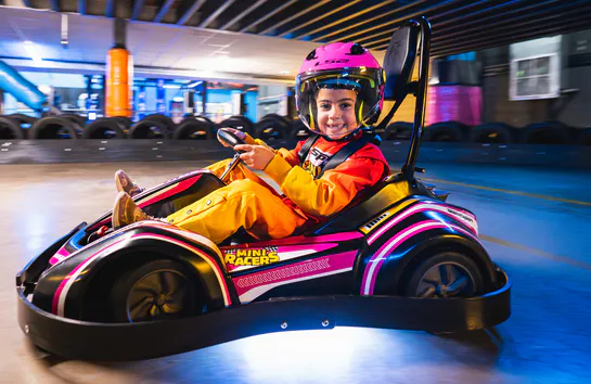 Mini racer aged 4–7 driving a go kart and smiling on the track