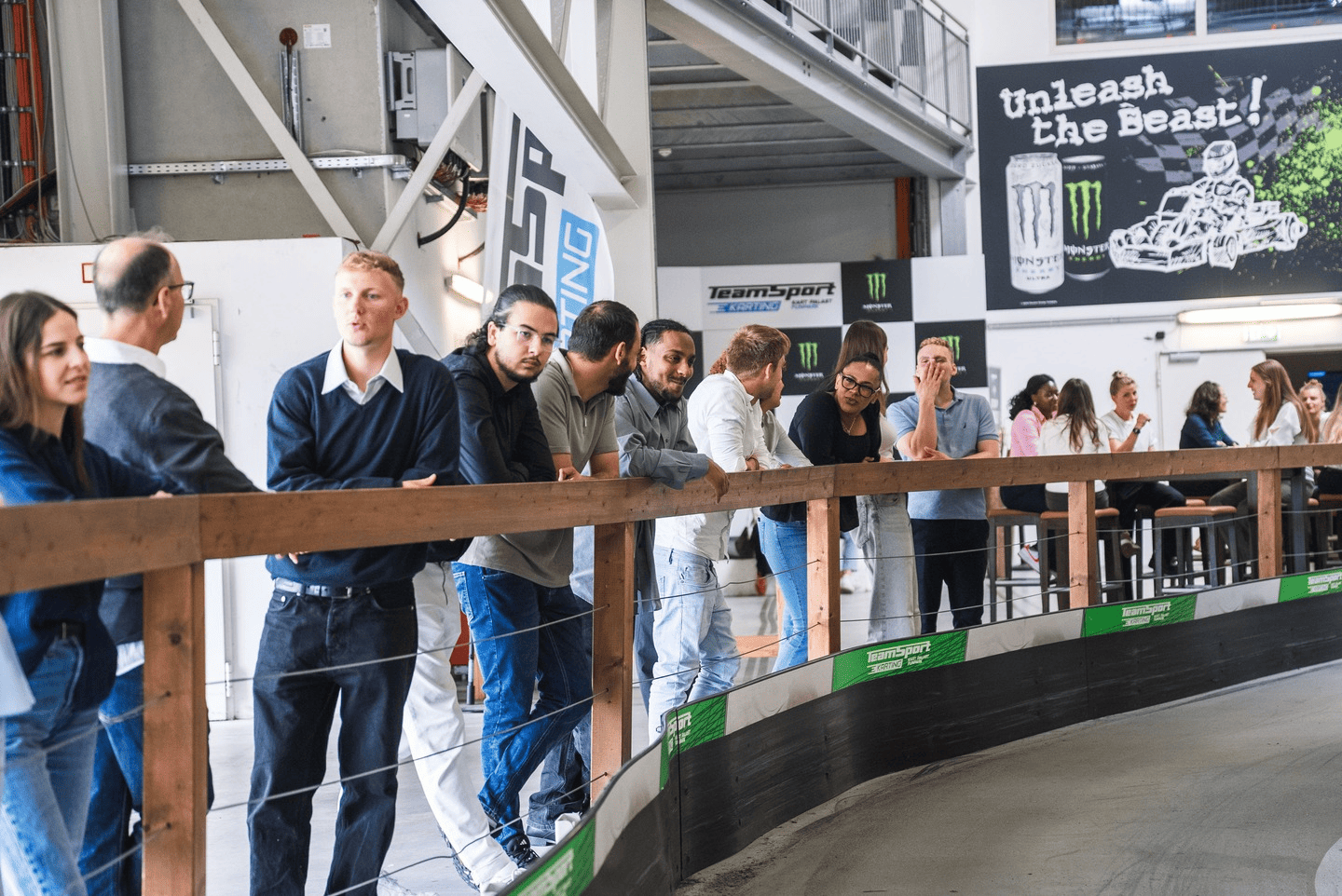 Eine Gruppe von Menschen steht im Zuschauerbereich der Rennstrecke und unterhält sich 