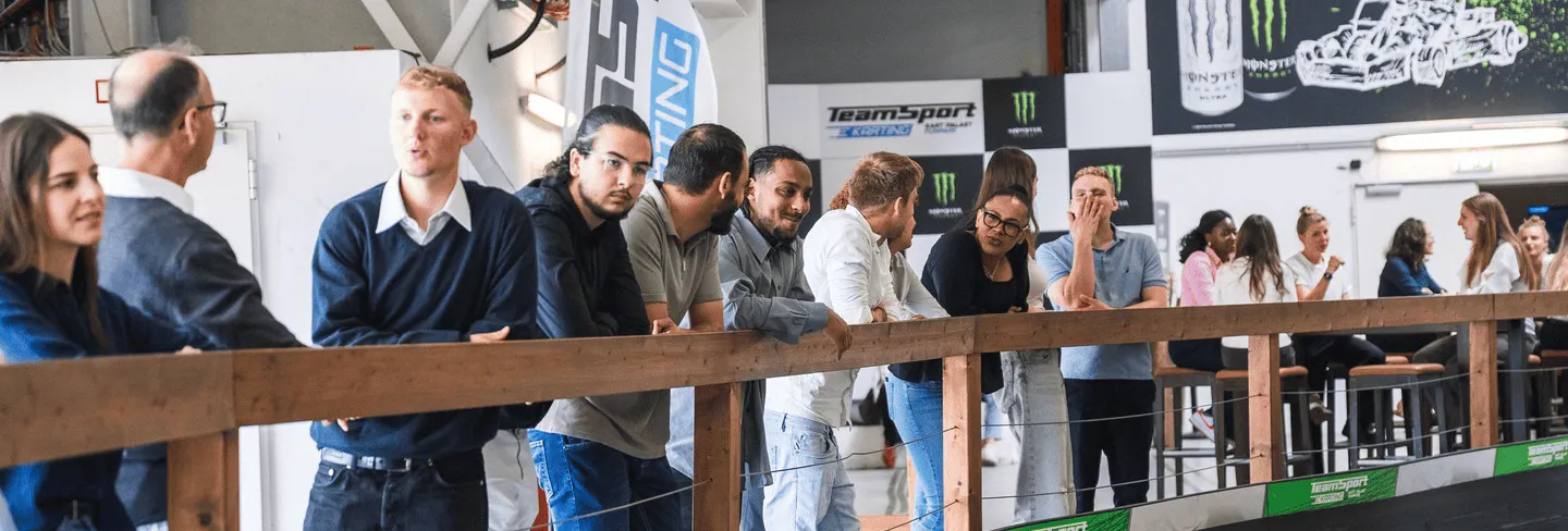 Eine Gruppe von Menschen steht im Zuschauerbereich der Rennstrecke und unterhält sich