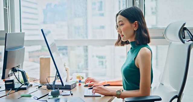 Young Asian businesswoman in casual clothing working financial data on computer sitting at desk in modern office. Sustainable business and finance. stock photo