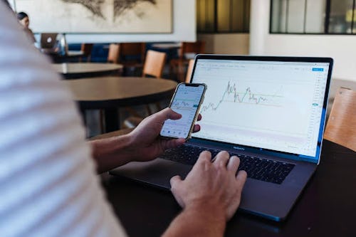 A man checking trading analytics using his phone and laptop