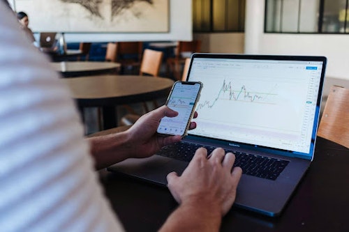 A man checking trading analytics using his phone and laptop