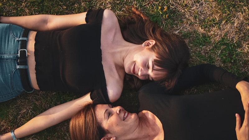 Mother and daughter lying on green grass staring into each other's eyes