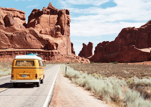 Image of a yellow mini-bus traveling on a lonely tarred road with mountains surrounding it