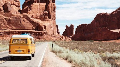 Image of a yellow mini-bus traveling on a lonely tarred road with mountains surrounding it