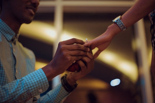 Image of a man on his knees putting on an engagement ring in a lady's finger