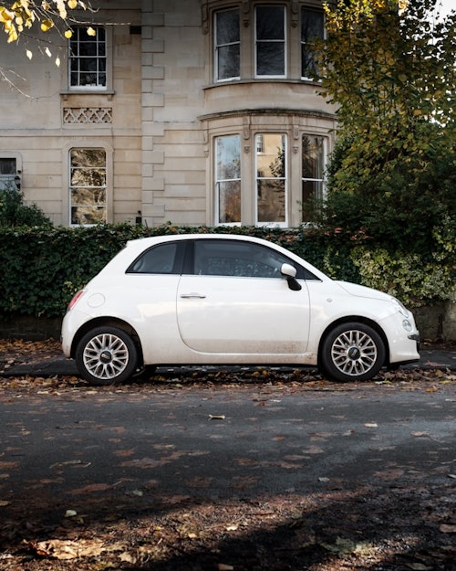 A small urban car parked in front of a classic mansion