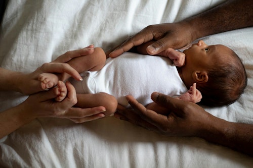 Interracial couple holding on a baby lying on a bed