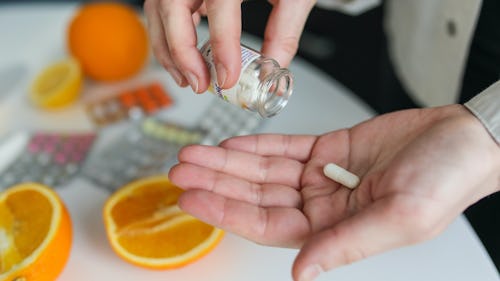 A woman taking folic acid supplement standing close to a table with oranges