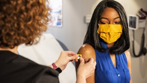 A white nurse giving a black woman vaccine injection in a hospital room