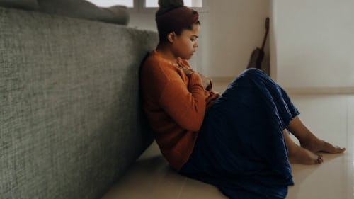 Image of a girl with anxiety sitting on the floor close to a bed with hands placed on her chest