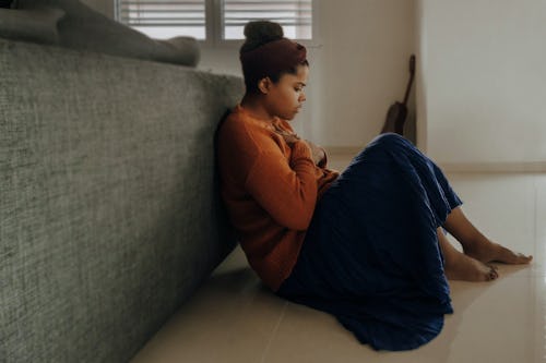 Image of a girl with anxiety sitting on the floor close to a bed with hands placed on her chest