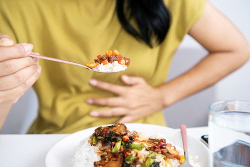 A woman with hands placed on her tummy while eating a full plate of rice and stew