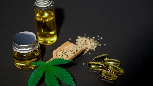 Image of a  cannabis plant, bottles of CBD oil and capsules on a table