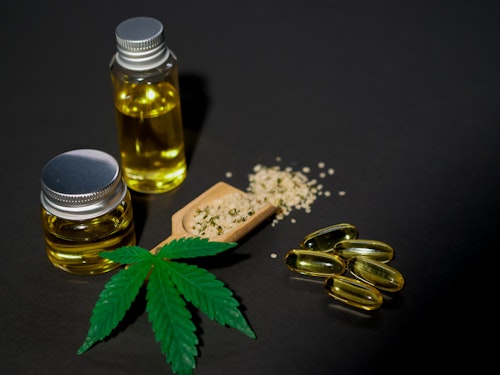 Image of a  cannabis plant, bottles of CBD oil and capsules on a table