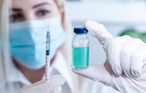 A nurse wearing nose mask holding a vaccine with syringe