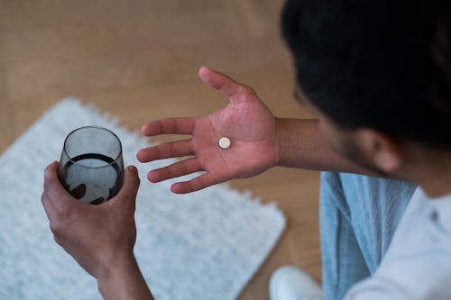 Image of a man holding a pill in one hand and a glass of water